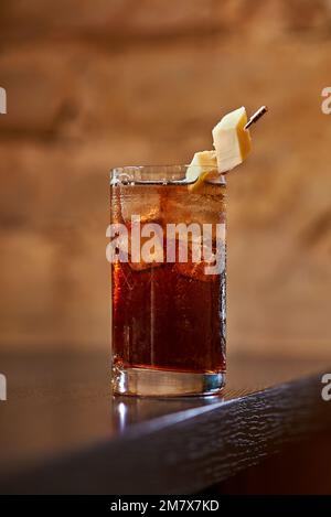 Cocktail di alcol marrone con cubetti di ghiaccio e formaggio sullo sfondo Foto Stock
