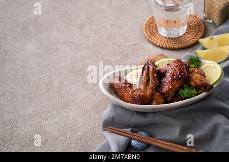 Primo piano delle ali di pollo teriyaki tostate e sauciate in un piatto bianco su sfondo grigio del tavolo. Foto Stock