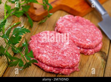 Cotolette di carne cruda con prezzemolo su tavola di legno Foto Stock