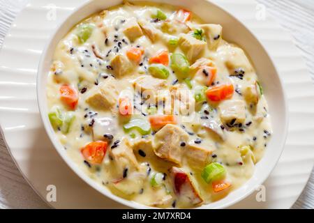 Zuppa cremosa di riso selvatico tacchino con patate rosse. carota, sedano, spezie ed erbe aromatiche in ciotola bianca su tavola di legno Foto Stock