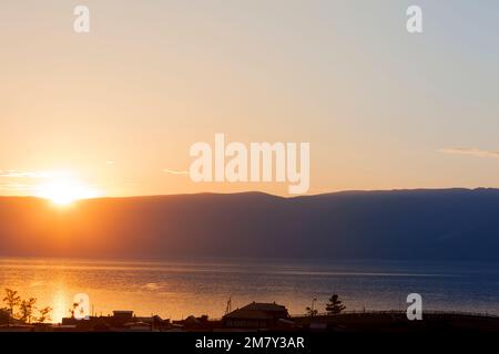 Tramonto sul lago Baikal sulle montagne all'orizzonte. Gli ultimi raggi di sole si riflettono nell'acqua per lasciar andare il buio della notte' Foto Stock