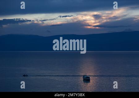 Tramonto sul lago Baikal sulle montagne all'orizzonte. Gli ultimi raggi di sole si riflettono nell'acqua per lasciar andare il buio della notte' Foto Stock