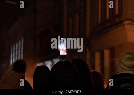 Smartphone con immagini sfocate su silhouette di persone durante gli spettacoli di fuoco nella piazza della città. Ucraina, Zhitomir, 22 novembre 2022 Foto Stock