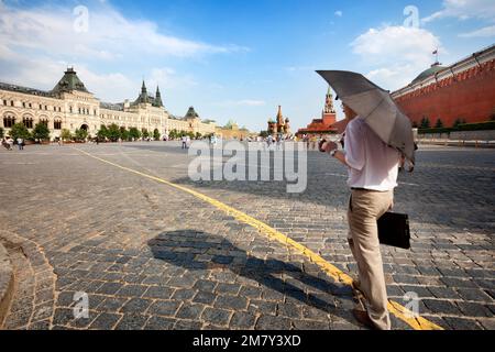 Mosca, Russia-20 luglio 2010: Un dirigente attraversa la Piazza Rossa di Mosca con un ombrello che protegge il caldo intenso di luglio e una piccola pioggia Foto Stock