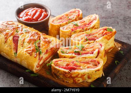 Deliziosa pizza stromboli rotolo farcito con salame salsiccia e mozzarella primo piano su un asse di legno sul tavolo. orizzontale Foto Stock