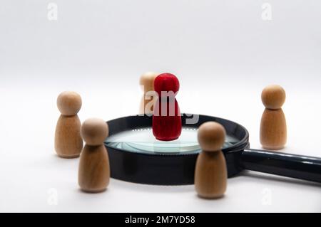 Bambola di legno rosso sulla parte superiore della lente d'ingrandimento circondata da un'altra figura di legno. concetto di leadership Foto Stock