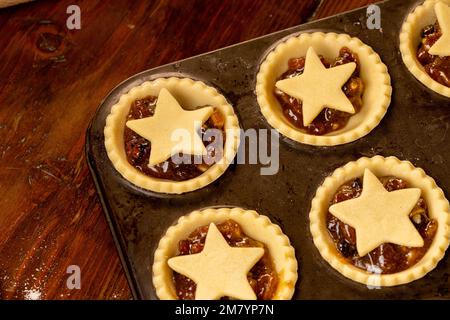 Primo piano di torte tritate sormontate da stelle in una teglia da forno di metallo scuro prima della cottura. Foto Stock