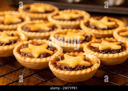 Primo piano di torte tritate sormontate da stelle di pasta che si raffreddano su una rastrelliera metallica. Natale casa cottura Foto Stock