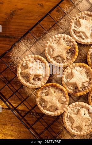 Piatto di torte di mince appena sfornate con stelle di pasticceria, spolverate con zucchero a velo su fondo di legno scuro: Cottura casalinga natalizia. Foto Stock