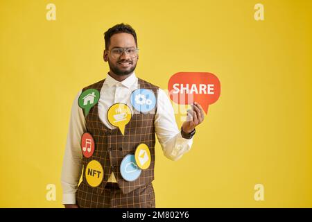 Uomo d'affari sorridente che mostra l'icona di condivisione, isolato su giallo Foto Stock