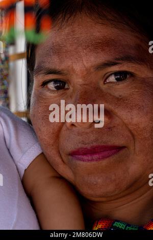 donna artigianale tradizionale che porta la figlia, circondata dal suo artigianato chaquira molto colorato Foto Stock