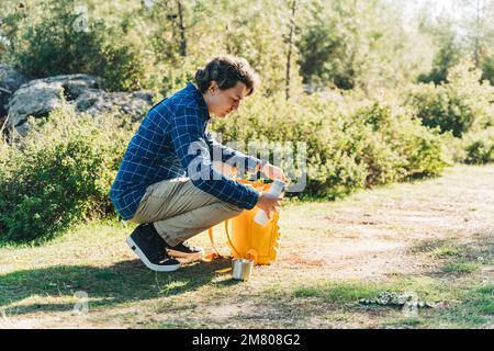 Adulto maschio turista con zaino giallo a piedi nella foresta. Giovane ragazzo in abiti casual con tazza di metallo e thermos durante le escursioni in estate greenwood Foto Stock