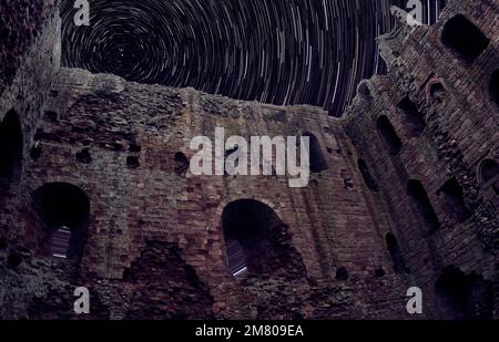 Castello di Norham in rovine con cielo notturno e sentieri stellari Foto Stock