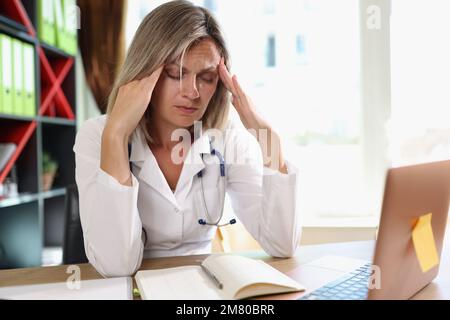 Medico di sesso femminile esausto che ha mal di testa durante il lavoro in clinica. Foto Stock