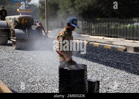 Un uomo cammina con asfalto fuso. Le strade sono pavimentate a mano a Mawlamyine, Myanmar Foto Stock