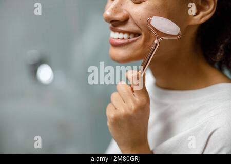 Primo piano della donna che fa il massaggio del viso utilizzando il rullo in bagno. Concetto naturale di cosmetica Foto Stock