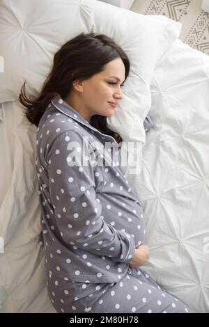 Donna incinta felice si trova sul letto matrimoniale e colpi di pancia Foto Stock