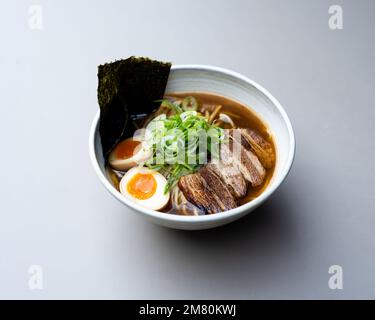 Zuppa asiatica di noodle, ramen con carne, tofu, verdure, nori e uova in ciotola bianca Foto Stock