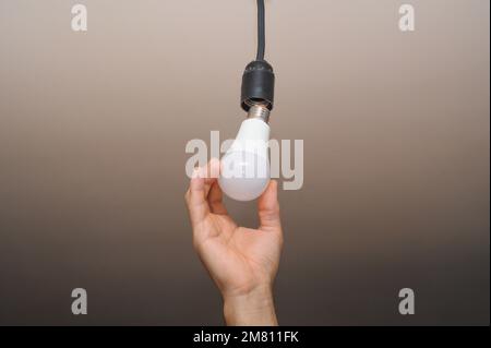 Installazione di ricambio LED elettrico. nella mano dell'uomo c'è una lampadina elettrica. Foto Stock