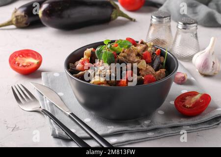 Stufato di carne con melanzane e pomodori servito in ciotola scura su sfondo grigio, primo piano Foto Stock