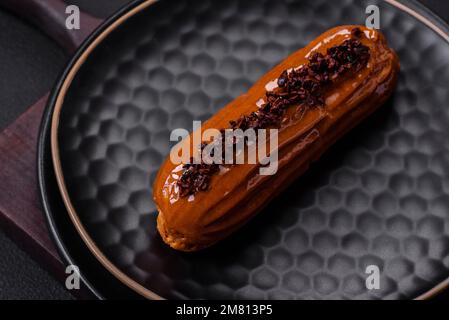 Delizioso eclair fresco con crema al cioccolato su un piatto di ceramica nera su fondo di cemento scuro Foto Stock