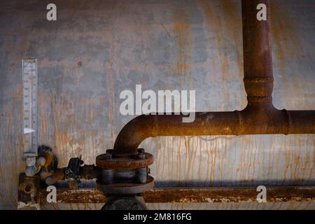 Tubi vecchi e arrugginiti e serbatoio dell'acqua in metallo con indicatore verticale. Foto Stock