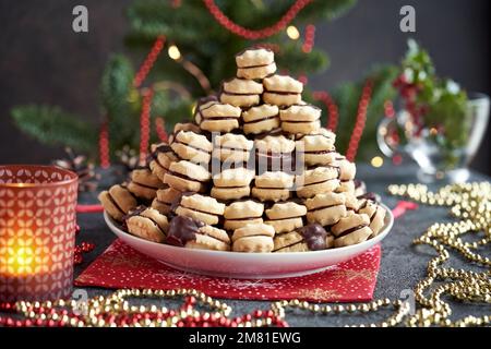 Un mucchio di biscotti di Natale fatti in casa ripieni di marmellata e immersi nel cioccolato, con decorazioni rosse e dorate Foto Stock