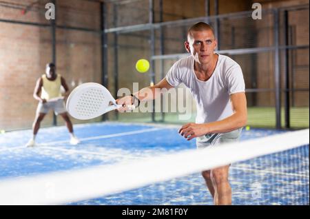 Uomo sportivo adulto che gioca il padel sul cortile interno Foto Stock