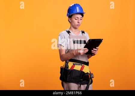 Ritratto di una donna ingegnere del settore che lavora con un tablet, alla ricerca di ispirazione per rinnovare online su gadget wireless. Appaltatore femminile in tute con dispositivo digitale elettronico. Foto Stock