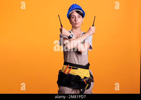 Donna operatrice che tiene i cacciaviti con entrambe le mani guardando la telecamera in studio. Imprenditore di costruzione femmina che fa il segno di arresto ed esprime il rifiuto o il rifiuto, forma di x. Foto Stock