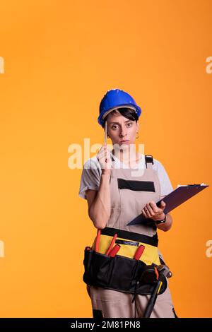 Le idee di brainstorming del costruttore femminile con gli articoli della clipboard in studio, prendendo le note sui lime e pensando a rinnovare la soluzione. Ingegnere industriale che utilizza le misurazioni per costruire il sito. Foto Stock