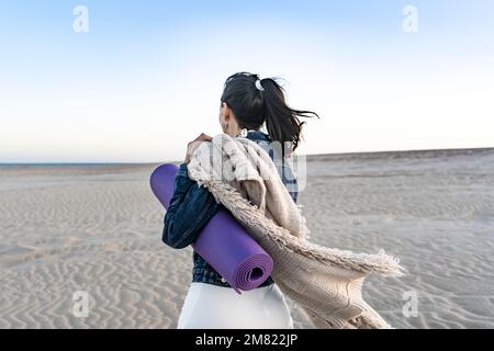 Donna che lascia la spiaggia mentre porta il suo tappetino Foto Stock