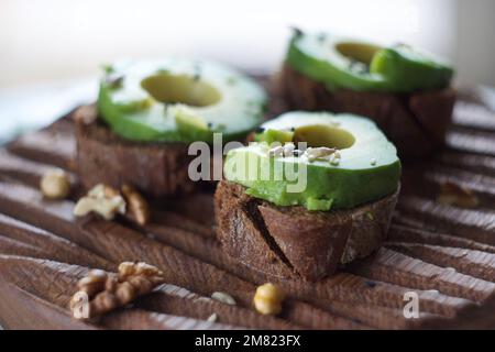 Tre panini avocado si trovano su un asse di legno Foto Stock