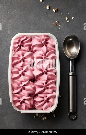 scatola aperta di gelato rosa e cucchiaio su sfondo grigio scuro, vista dall'alto Foto Stock