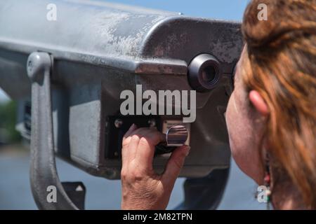 Vista ravvicinata di una donna matura latina attraverso binocoli pubblici. Concetti di curiosità, osservazione, esplorazione, ricerca, viaggio. Foto Stock