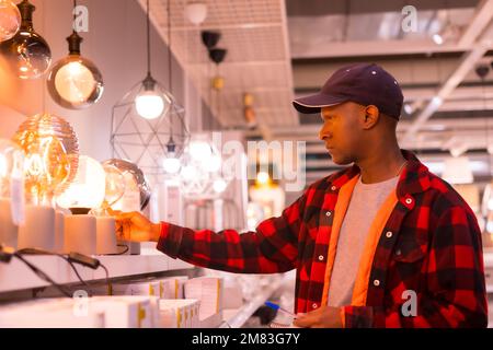 Un uomo nero africano che indossa un abito elegante visto shopping di lampade in un supermercato Foto Stock