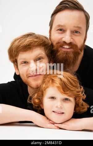 ritratto di famiglia di capretto rosso con papà e nonno barbuto sorridente alla macchina fotografica su sfondo grigio chiaro, immagine di scorta Foto Stock