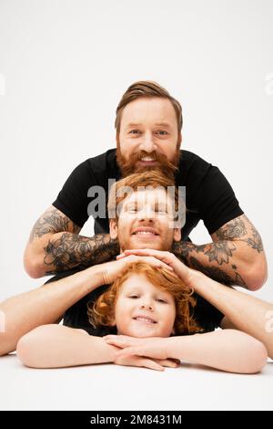 ritratto di famiglia di uomini redhead e ragazzo allegro posa su sfondo grigio chiaro, immagine stock Foto Stock