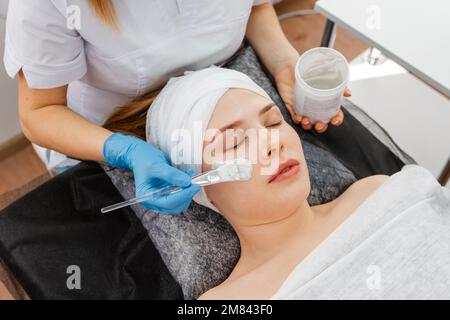 Cosmetician dando cliente maschera facciale per la cura della pelle. Lavoro di estetista Foto Stock