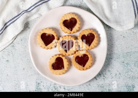 Biscotti a forma di cuore su piastra su sfondo grigio. Biscotti con marmellata al centro. Dessert da forno. Vista dall'alto Foto Stock