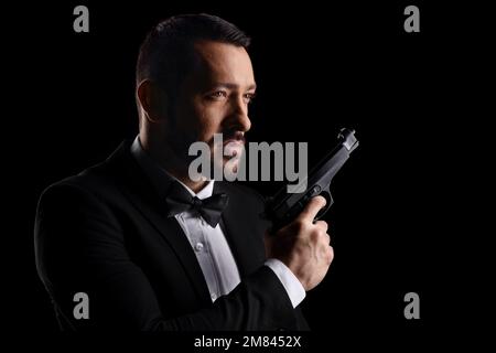 Uomo con cravatta ad arco che tiene una pistola isolata su sfondo nero Foto Stock