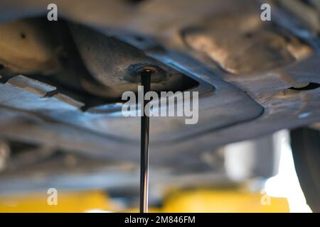 Un primo piano della parte dell'automobile mentre controlla e cambia l'olio motore contro uno sfondo sfocato Foto Stock