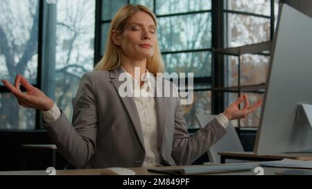 Calma caucasica di mezza età adulta consapevolezza donna matura business donna rilassato donna d'affari imprenditore lavoratore datore di lavoro in ufficio a tavola Foto Stock