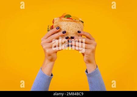 Le mani di una donna che tiene un panino su sfondo giallo Foto Stock