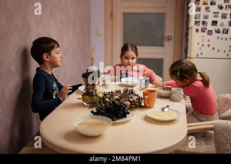 Tre bambini cenano insieme in cucina. Foto Stock