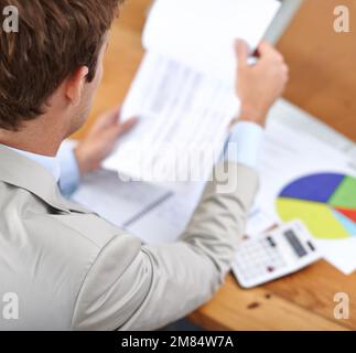 Ci deve essere un senso tagliare sulle spese... un uomo d'affari che rivede le figure mentre si siede alla sua scrivania. Foto Stock