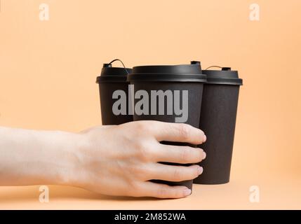 Mano donna che tiene una tazza nera da take away del caffè su fondo pastello neutro. Foto Stock