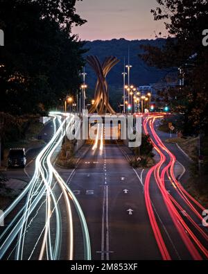 Un lungo scatto verticale di luci per auto sentieri su una strada vicino a una rotonda del centro con una scultura d'arte a Bonn, Germania Foto Stock