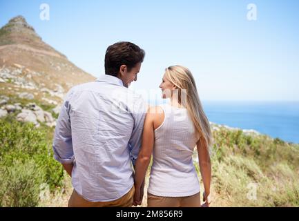 Il tuo amore mi fa sentire in cima al mondo. una giovane coppia felice in piedi mano sul pendio di una montagna. Foto Stock