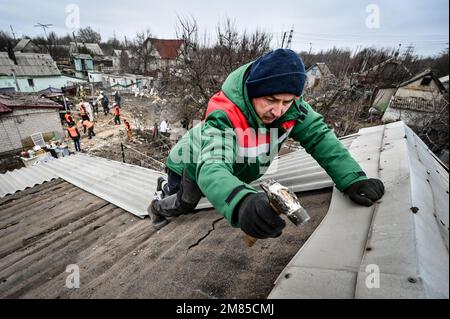 ZAPORIZHZHZHIA, UCRAINA - 12 GENNAIO 2023 - Un operatore di servizi di pubblica utilità sostituisce un foglio di cemento in fibra ondulata sul tetto di una delle 39 case danneggiate in un Foto Stock